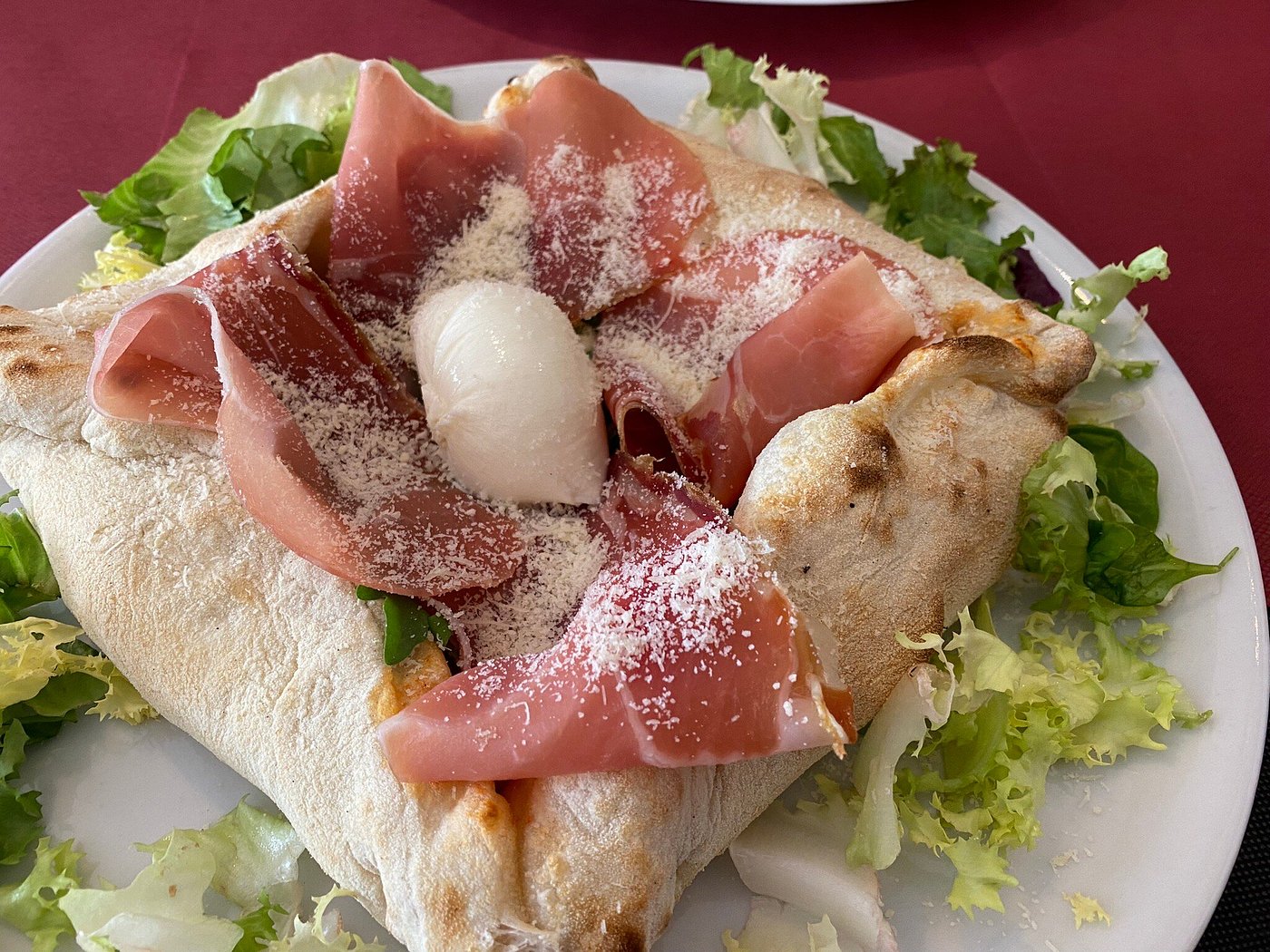 Calzone al horno abierto con prosciutto crudo, mozzarella y queso rallado sobre cama de ensalada